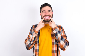 Strong healthy straight white teeth. Close up portrait of happy young caucasian man wearing plaid shirt over white background with beaming smile pointing on perfect clear white teeth.