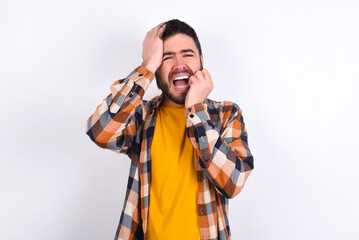 Gloomy young caucasian man wearing plaid shirt over white background, hiding face with hands pouting and crying, standing upset and depressed complaining about job problem.