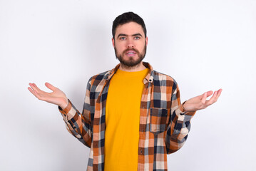 young caucasian man wearing plaid shirt over white background looks uncertain shrugs shoulders.