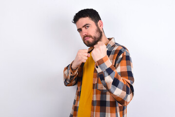 Portrait of attractive young caucasian man wearing plaid shirt over white background holding hands in front of him in boxing position going to fight.