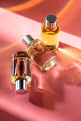 Transparent bottles of perfume on a pink background. Natural light and shadows. Women's and men's...