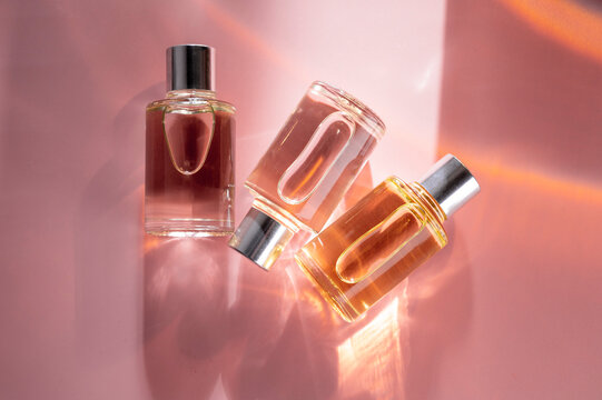 Transparent bottles of perfume on a pink background. Natural light and shadows. Women's and men's essence concept
