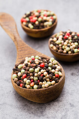 Peppercorn mix in a wooden bowl on grey table.