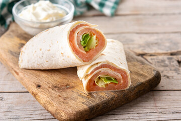 Salmon wrap sandwich roll with cheese and vegetables on wooden table	