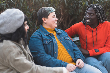 Multiethnic group of women carefree talking together sitting on a bench in the park - concept of...