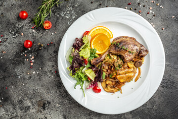 duck leg confit meat portion of prepared with baked potatoes, mushrooms and onions, top view