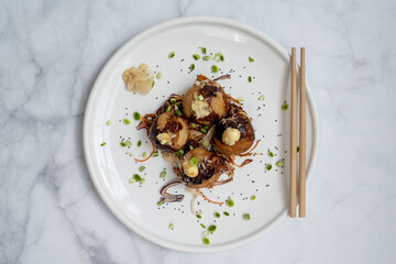 A plate of takoyaki with chopsticks over a marble table