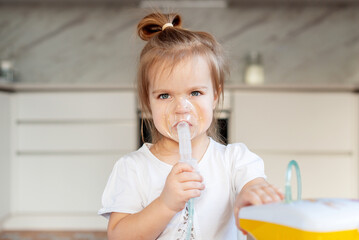 Little caucasian girl is breathing with special mask, which helps to stop asthma attack or relieve symptoms of respiratory disease. Child making inhalation with nebulizer at home