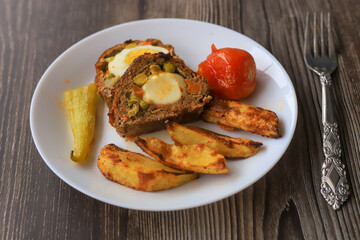 Meatloaf with egg and peas inside. Potato slices , tomatoes , peppers on the plate.
