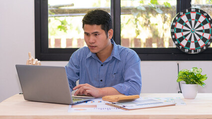 Fototapeta premium Handsome, smart Asian businessman working from home in the office. Computing reports. Paperwork financiers. use a laptop and a calculator