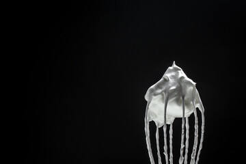 Metal whisk for whipping eggs with cream white raw meringue for perfect peaks isolated on black. Whipped cream, cookie recipe