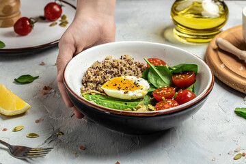 Woman mixing delicious superfood salad quinoa, avocado, egg, tomatoes, spinach and sunflower seeds on light background. Healthy food, ketogenic diet, diet lunch concept, place for text, top view