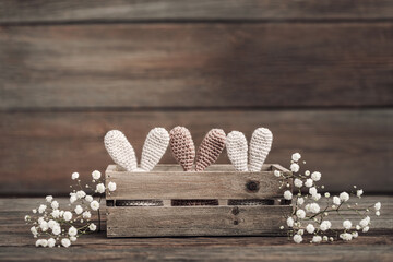 Three Easter eggs in crocheted hats with rabbit ears in a wooden box on a rustic wooden table.