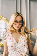 Portrait of attractive caucasian young woman in eyeglasses standing in bedroom near mirror.