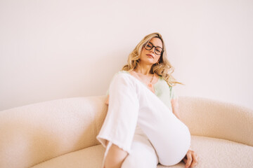 Portrait of young attractive stylish caucasian woman in eyeglasses sitting on a sofa.