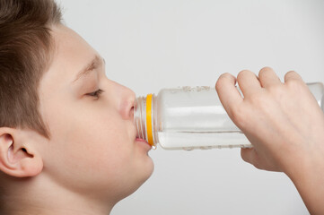 A caucasian boy holding a bottle of drinking water taking a sip