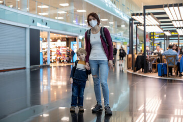 Fototapeta premium Cute baby boy waiting boarding to flight in airport transit hall near departure gate. Active family lifestyle travel by air with children
