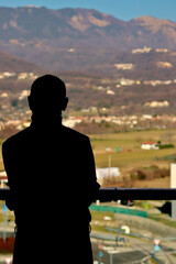 Male silhouette looking out of the window at a blurred mountain panorama in Veneto (Schio, Vicenza)