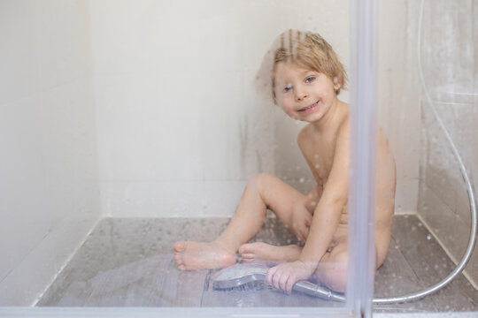 Blond child, sweet toddler boy in bathroom, taking shower, sitting on the floor, punished
