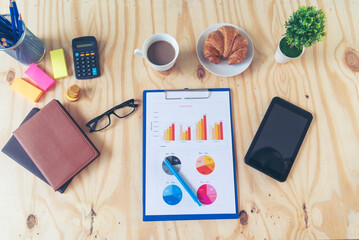 Naklejka premium Office laptop business financial document chart and graph on wooden table with coffee cup. Flat lay notebook computer laptop on office desk. No people business graph chart mockup on business workspace