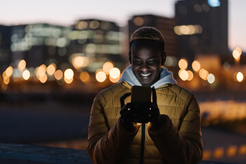 Young happy african man using cell phone in the city at night
