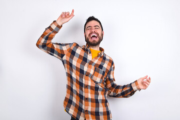 Naklejka premium Photo of upbeat young caucasian man wearing plaid shirt over white background has fun and dances carefree wear being in perfect mood makes movements. Spends free time on disco party