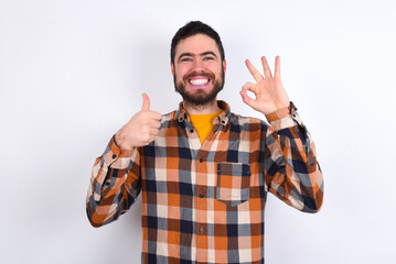 young caucasian man wearing plaid shirt over white background smiling and looking happy, carefree and positive, gesturing victory or peace with one hand