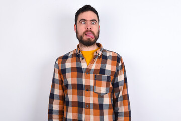 Fototapeta premium Funny young caucasian man wearing plaid shirt over white background makes grimace and crosses eyes plays fool has fun alone sticks out tongue.