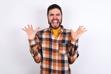 Crazy outraged young caucasian man wearing plaid shirt over white background screams loudly and gestures angrily yells furiously. Negative human emotions feelings concept