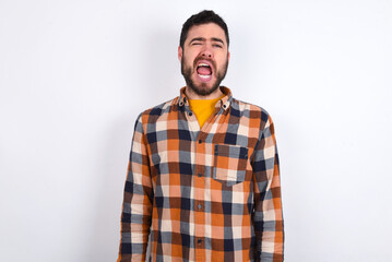 young caucasian man wearing plaid shirt over white background yawns with opened mouth stands. Daily morning routine