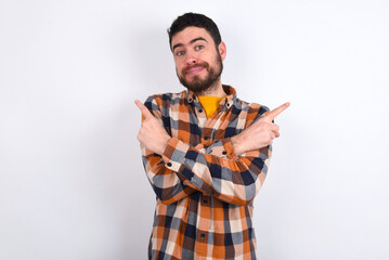 young caucasian man wearing plaid shirt over white background crosses arms and points at different sides hesitates between two items or variants. Needs help with decision