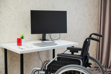 Workplace for a disabled person. Wheelchair at the table with a computer. 