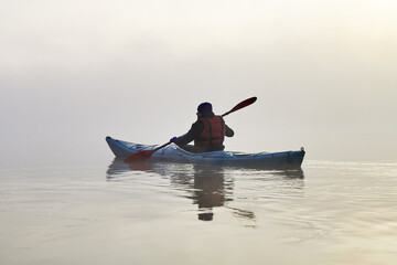 Alone man paddle kayak in the fog through dense haze in Danube river at autumn morning