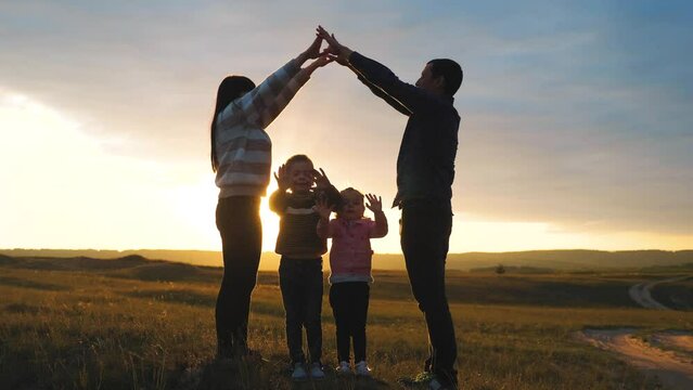 happy family. teamwork adult parents and small children shows a house and comfort symbol silhouette at sunset. happy family mom lifestyle dad and kids children portray a house roof hold their hands