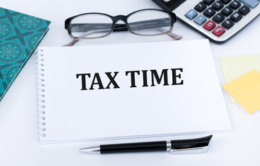 tax time text on notepad on a white background next to glasses, calculator and documents