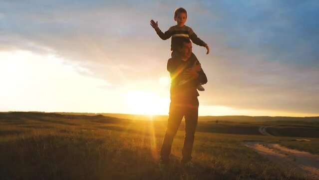 happy family. son sits on his neck teamwork at father shows hands to the side plays at the pilot depicts an airplane silhouette at sunset. happy family lifestyle concept childhood man dad with little