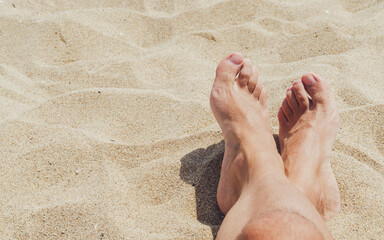 Feet of young man sunbathing on the beach sand.