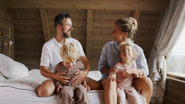 Happy young family with small children having fun in bed on holiday.