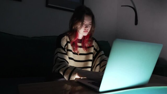 Young woman watching media or working on a laptop at night in the darkness with copyspace