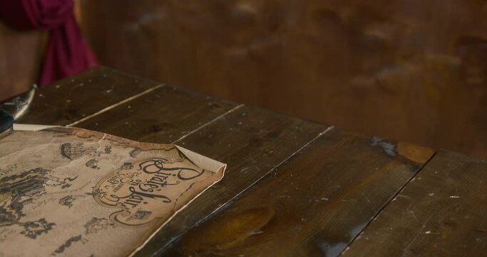 Pirate takes loaded revolver lying on wooden table near old sea yellowed treasure map IN cabin of pirate ship at voyage close view