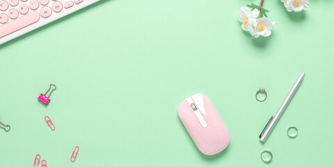 Workplace of an office worker. Keyboard, mouse, stationery and spring flowers. Green pastel background. Top view, flat lay, banner.