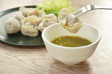 steamed fish dumpling stabbing in fork dipping spicy and sour sauce