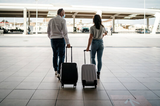 Man and woman with luggage wearing protective masks  leaving the airport