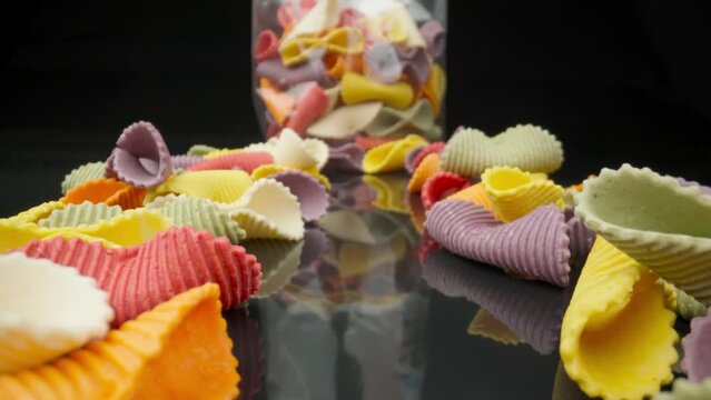 Creative multicolored pasta farfalle on a black background in perspective with packaging in background. Moving extreme macro