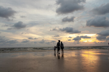 Father and mother and children playing together outdoor on beach. Happy family travel on beach in holiday, Summer vacations. Happy family are having fun on a tropical beach in sunset and cloudy. 
