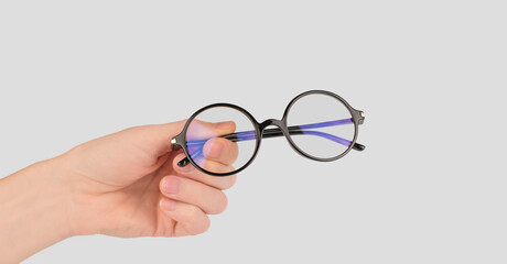 Round stylish glasses for vision in a male hand on a gray background, copy space