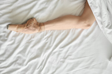Woman in pointe shoe shows her leg from under coverlet