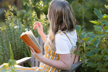 Beautiful blonde woman in a green summer garden on a chaise longue. A girl in a yellow sundress and...