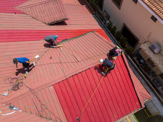A team of roofers or carpenters installs new corrugated metal roofing with ribbed sheet design on a...