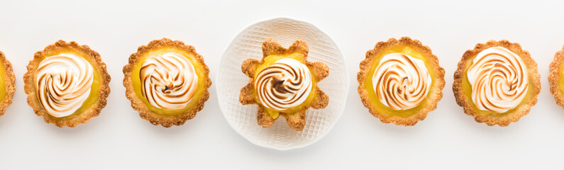 Narrow top down view of a row of homemade lemon meringue tartlets.